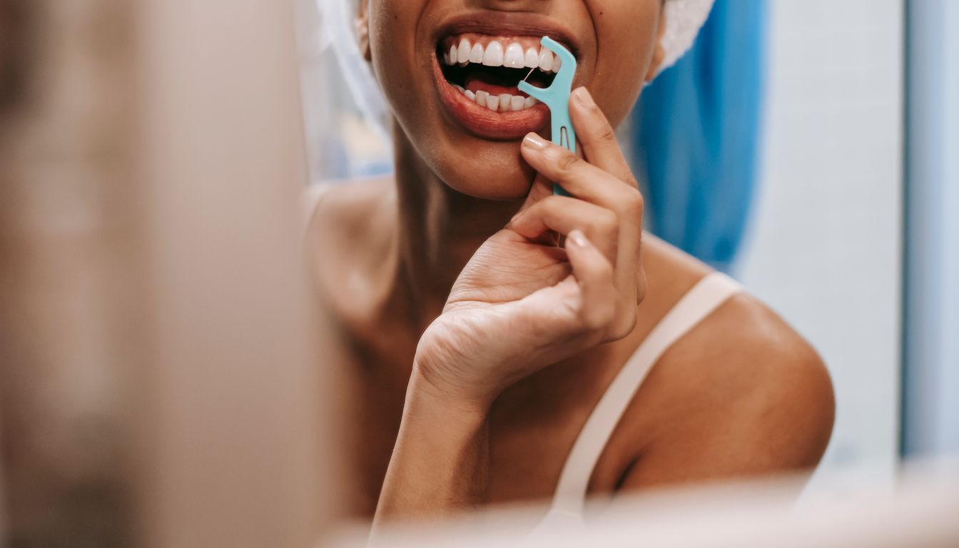 Woman flossing her teeth in front of a bathroom mirror